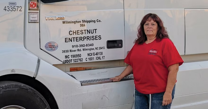 April Crysel, a professional truck driver for Chestnut Enterprises, standing proudly in front of a semi-truck, recognized as Women In Trucking’s December 2024 Member of the Month.